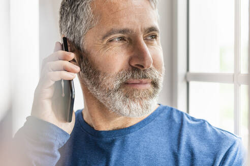Älterer Geschäftsmann, der im Stehen zu Hause mit seinem Handy telefoniert - SBOF02568