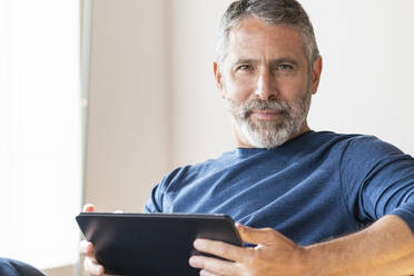 Confident businessman using digital tablet while sitting at home - SBOF02572