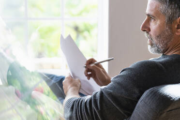 Thoughtful businessman holding paper while sitting at home - SBOF02584