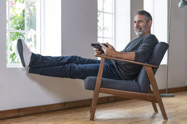 Smiling businessman using digital tablet while sitting on armchair at home - SBOF02586