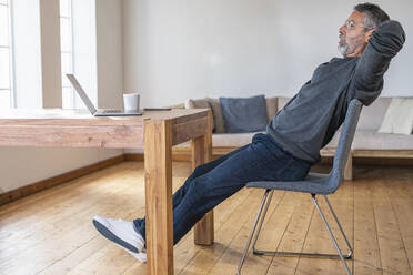 Businessman resting while sitting with hands behind head at home office - SBOF02607