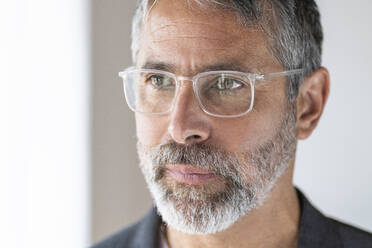 Close-up of mature businessman wearing eyeglasses looking away while standing at home - SBOF02618