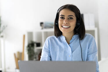 Kundendienstmitarbeiter mit Headset lächelnd bei der Verwendung eines Laptops im Büro - GIOF10885