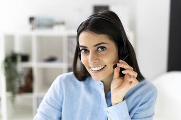 Smiling businesswoman adjusting headset while sitting at office - GIOF10904
