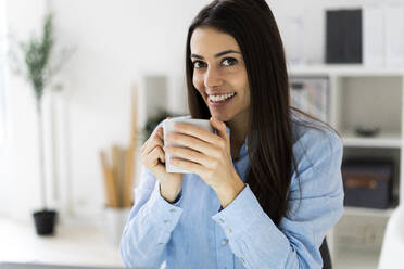 Smiling businesswoman drinking coffee while sitting at office - GIOF10905