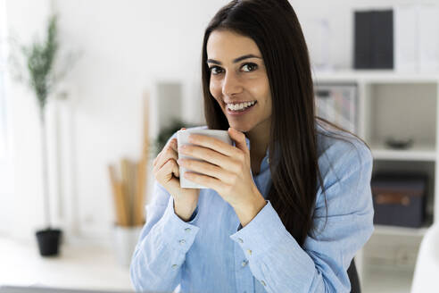 Lächelnde Geschäftsfrau, die im Büro sitzend Kaffee trinkt - GIOF10905