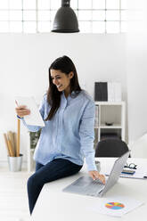Geschäftsfrau, die an einer Telefonkonferenz auf einem digitalen Tablet teilnimmt, während sie im Büro am Laptop sitzt - GIOF10916