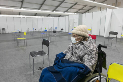 Ältere Frauen mit Schutzmaske und warmer Kleidung sitzen im Rollstuhl im Impfzentrum - NDF01208