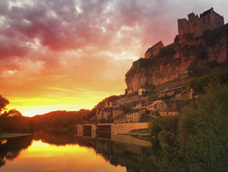 France, Dordogne, Beynac-et-Cazenac, Riverside village at sunset with Chateau de Beynac castle looming in background - GWF06849