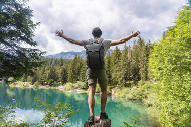 Unbeschwerter Mann mit Rucksack steht mit ausgestreckten Armen am Caumasee im Kanton Graubünden, Schweiz - TAMF02816