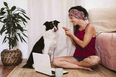 Frau füttert Haustier mit Wassermelone, während sie zu Hause am Laptop sitzt - EBBF02337