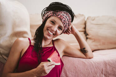 Frau lächelnd beim Essen Wassermelone zu Hause sitzen - EBBF02341