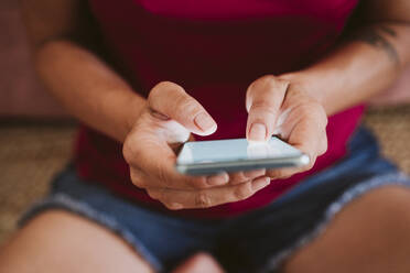 Woman using smart phone while sitting at home - EBBF02353