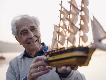 Lächelnder Mann, der im Freien stehend ein Segelschiff-Spielzeug untersucht - GUSF05037