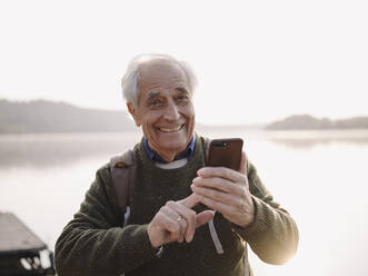 Smiling senior man using mobile phone while standing against sky - GUSF05047