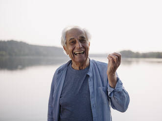 Happy man singing while standing against lake - GUSF05060