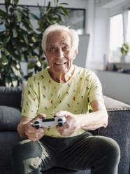 Älterer Geschäftsmann spielt ein Handheld-Videospiel, während er auf dem Sofa im Büro sitzt - GUSF05093