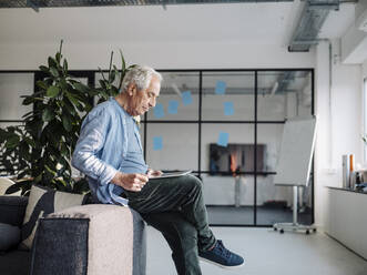 Businessman using digital tablet while sitting on sofa at office - GUSF05097