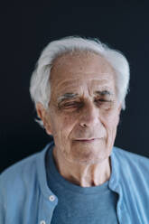 Senior man standing with eyes closed against black background - GUSF05118