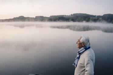Älterer Mann schaut auf die Aussicht, während er am See steht - GUSF05121