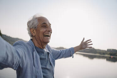 Unbekümmerter älterer Mann steht mit ausgestreckten Armen vor dem Himmel - GUSF05146