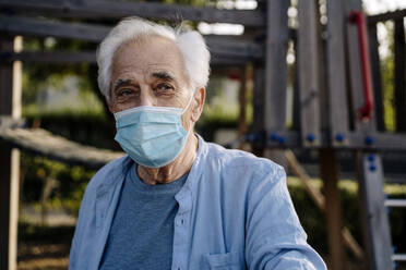 Älterer Mann mit Schutzmaske, der im Park steht und starrt - GUSF05153