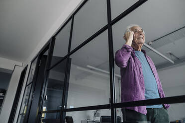 Älterer Geschäftsmann, der im Büro stehend mit seinem Handy telefoniert - GUSF05159