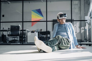 Geschäftsmann mit Virtual-Reality-Headset beim Entspannen auf dem Boden im Büro - GUSF05165