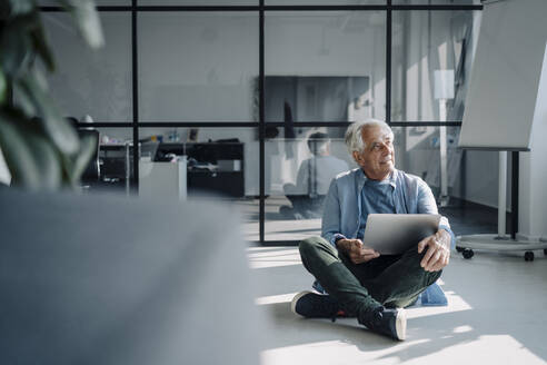 Älterer Unternehmer schaut weg, während er mit einem Laptop im Büro sitzt - GUSF05166