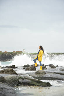 Young woman wearing yellow looking at view while standing on rock - KBF00695