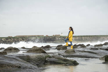 Woman looking at view while standing on coastline rock - KBF00696