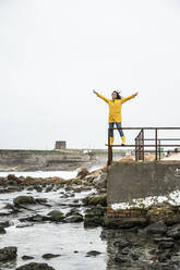 Carefree woman with arms outstretched standing on railing - KBF00698