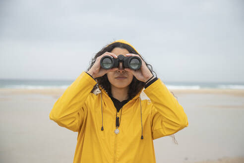 Woman using binoculars while standing at beach - KBF00703