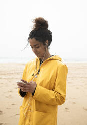Lächelnde Frau, die am Strand steht und ein Mobiltelefon benutzt - KBF00707