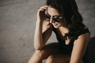 Thoughtful woman sitting on concrete footpath during sunny day - LHPF01350