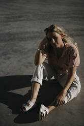 Relaxed woman with eyes closed sitting on concrete footpath - LHPF01354