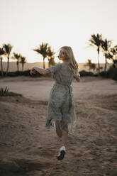 Happy woman in mid air while dancing over sand during sunset - LHPF01369