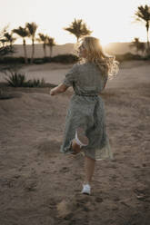 Cheerful woman dancing on beach while looking away during sunset - LHPF01370