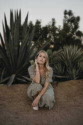 Beautiful woman crouching against cactus plants during sunset - LHPF01372
