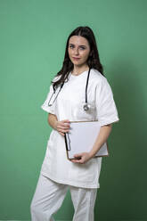 Young female doctor with clipboard and stethoscope by green background - GIOF10933