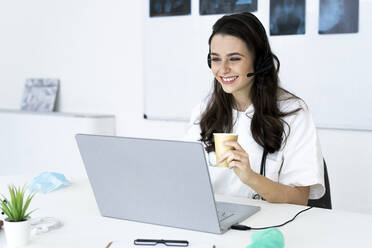 Happy female doctor consulting online through laptop at desk - GIOF10955