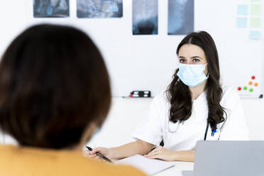 Ärztin im Gespräch mit einem Patienten in der Klinik während COVID-19 - GIOF10961