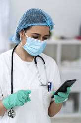 Young female doctor with surgical cap using smart phone in clinic - GIOF10983