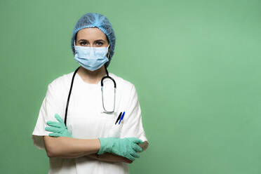 Female doctor with arms crossed against green background in studio - GIOF10986