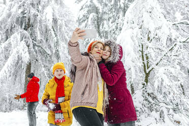 Mutter und Tochter nehmen Selfie durch Handy, während stehend mit Familie im Hintergrund im Wald - OGF00810