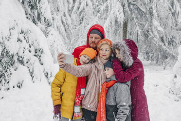 Reife Frau, die selfie mit Familie beim Stehen im Wald während snowing - OGF00811