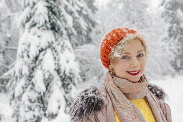 Mature woman smiling while standing in forest during winter - OGF00817