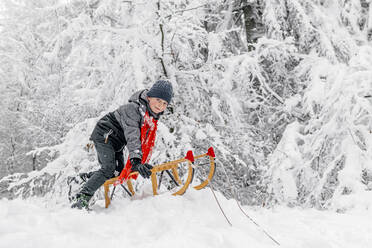 Junge beim Schlittenfahren mit Holzschlitten auf Schnee im Wald - OGF00827