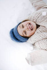 Cheerful girl with scarf lying on snow during winter - KMKF01507