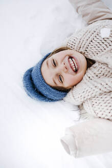 Fröhliches Mädchen mit Schal, das im Winter im Schnee liegt - KMKF01507